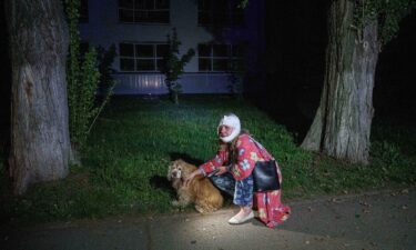 An injured woman sits with her dog near a house destroyed by a Russian airstrike.