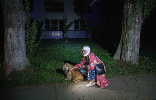 An injured woman sits with her dog near a house destroyed by a Russian airstrike.
