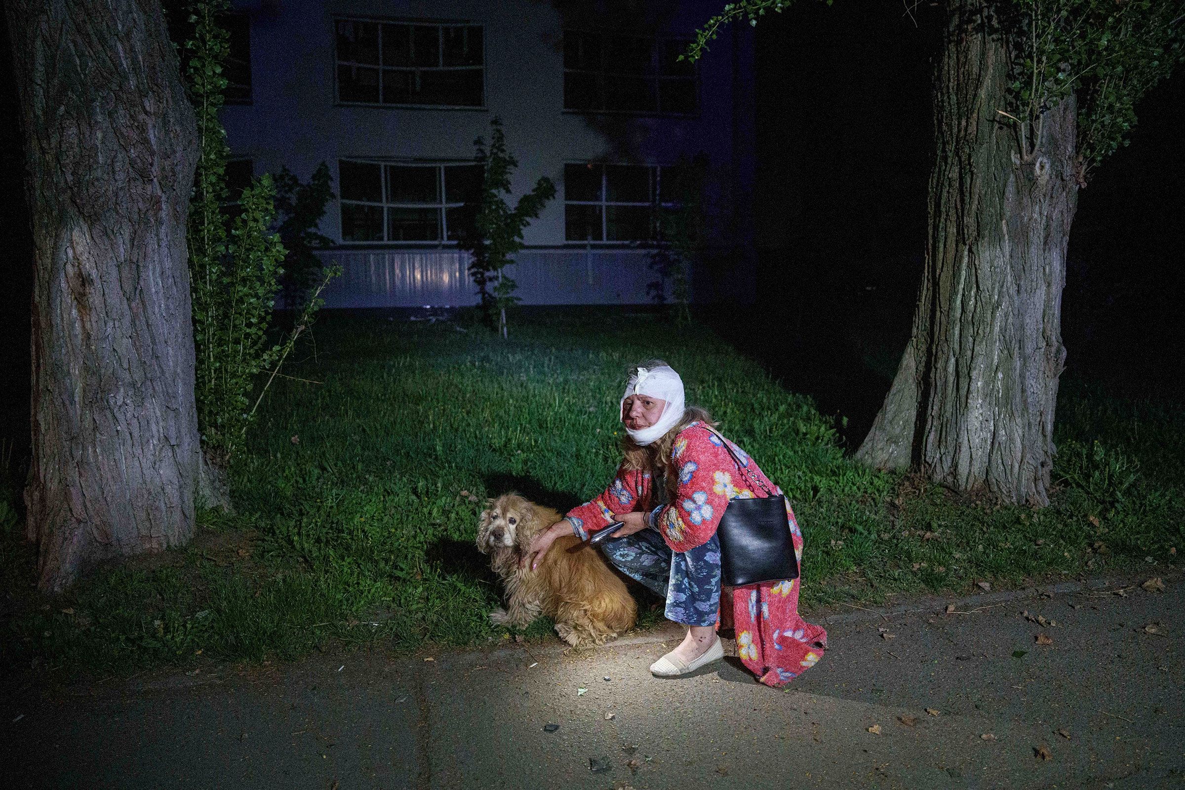 <i>Evgeniy Maloletka/AP via CNN Newsource</i><br/>An injured woman sits with her dog near a house destroyed by a Russian airstrike.